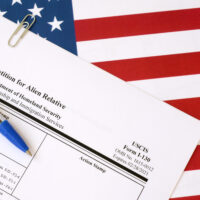 I-130 Petition for alien relative blank form lies on United States flag with blue pen from Department of Homeland Security close up