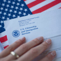 Letter (Envelope) from USCIS and left hand on flag of USA background.