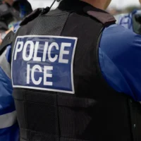 Ice Police Agent - officer of Immigration and Customs Enforcement. Close-up of POLICE ICE marking on the back of a stab proof vest worn by a trio of police officers at the scene of immigrant incident.