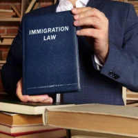 a-person-in-a-suit-holds-a-book-titled-immigration-law-in-front-of-a-bookshelf